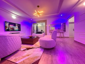 Una sala moderna con una televisión de pantalla plana, un sofá, una mesa de centro y un otoman redonda.