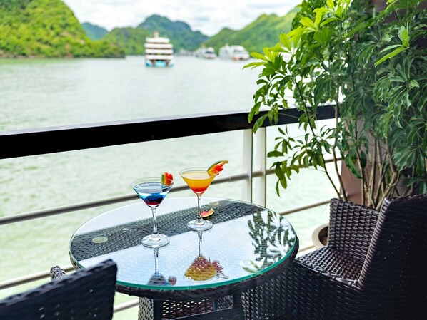 A table with two drinks on a balcony overlooking a body of water with boats.