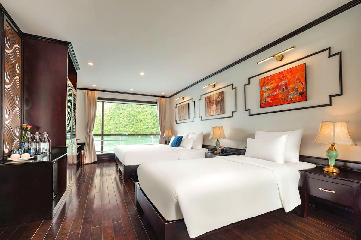 Una habitación de hotel con dos camas, un ventanal grande y obras de arte en las paredes.