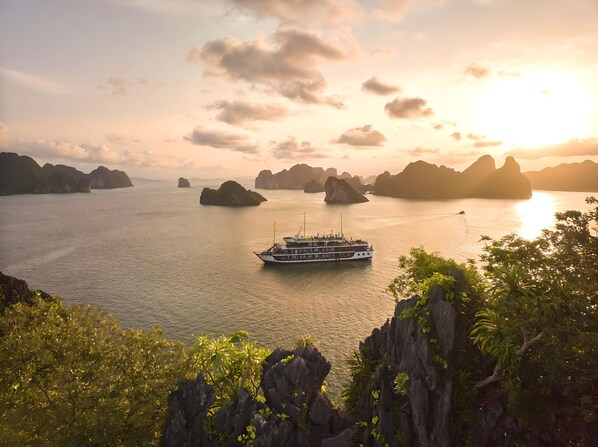 Un bateau sur des eaux calmes, avec des îles rocheuses en arrière-plan et une végétation luxuriante au premier plan.