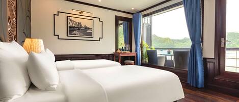 A hotel room with a large bed, a desk with a chair, a window with curtains, and a view of greenery.