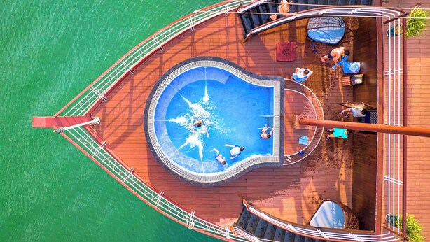 Eine Vogelperspektive auf ein Boot mit einem zentralen Swimmingpool, umgeben von einem Deck mit Sitzgelegenheiten und einer Geländer.
