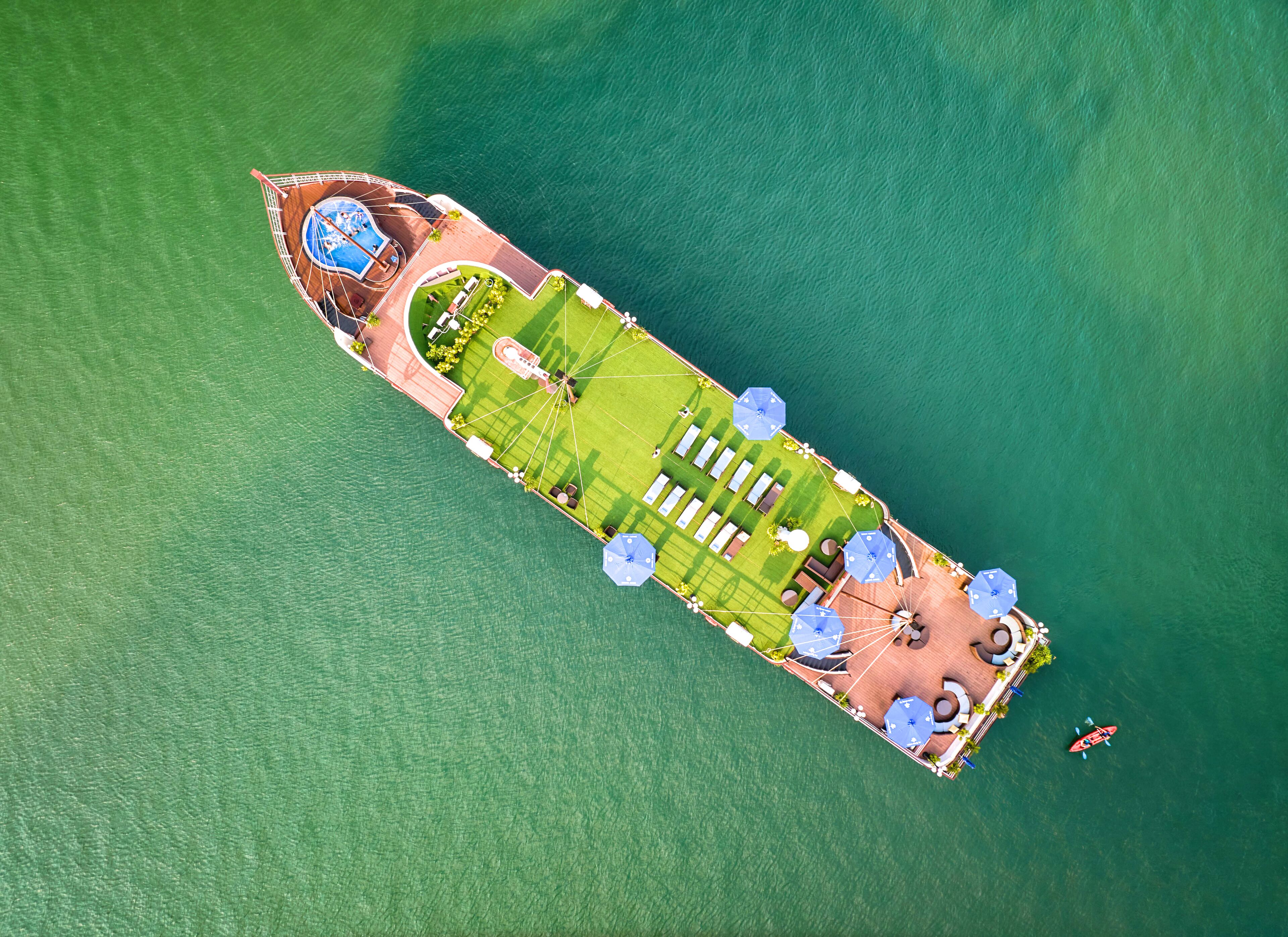 An aerial view of a yacht with a swimming pool, sun loungers, and a small boat.