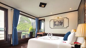 Ein Hotelzimmer mit einem großen Bett, Blick ins Freie, einem Schreibtisch mit Stuhl und einer Zimmerpflanze.