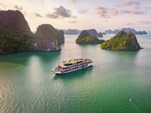 Un grand bateau doté de plusieurs ponts, dont un pont supérieur couvert, voguant sur une mer turquoise et calme, entouré d’îles verdoyantes.