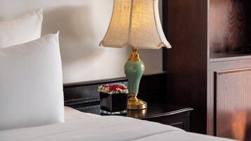 A neatly made bed with white linens, a green lamp with a gold base, and a small vase with red and white flowers on a dark nightstand.