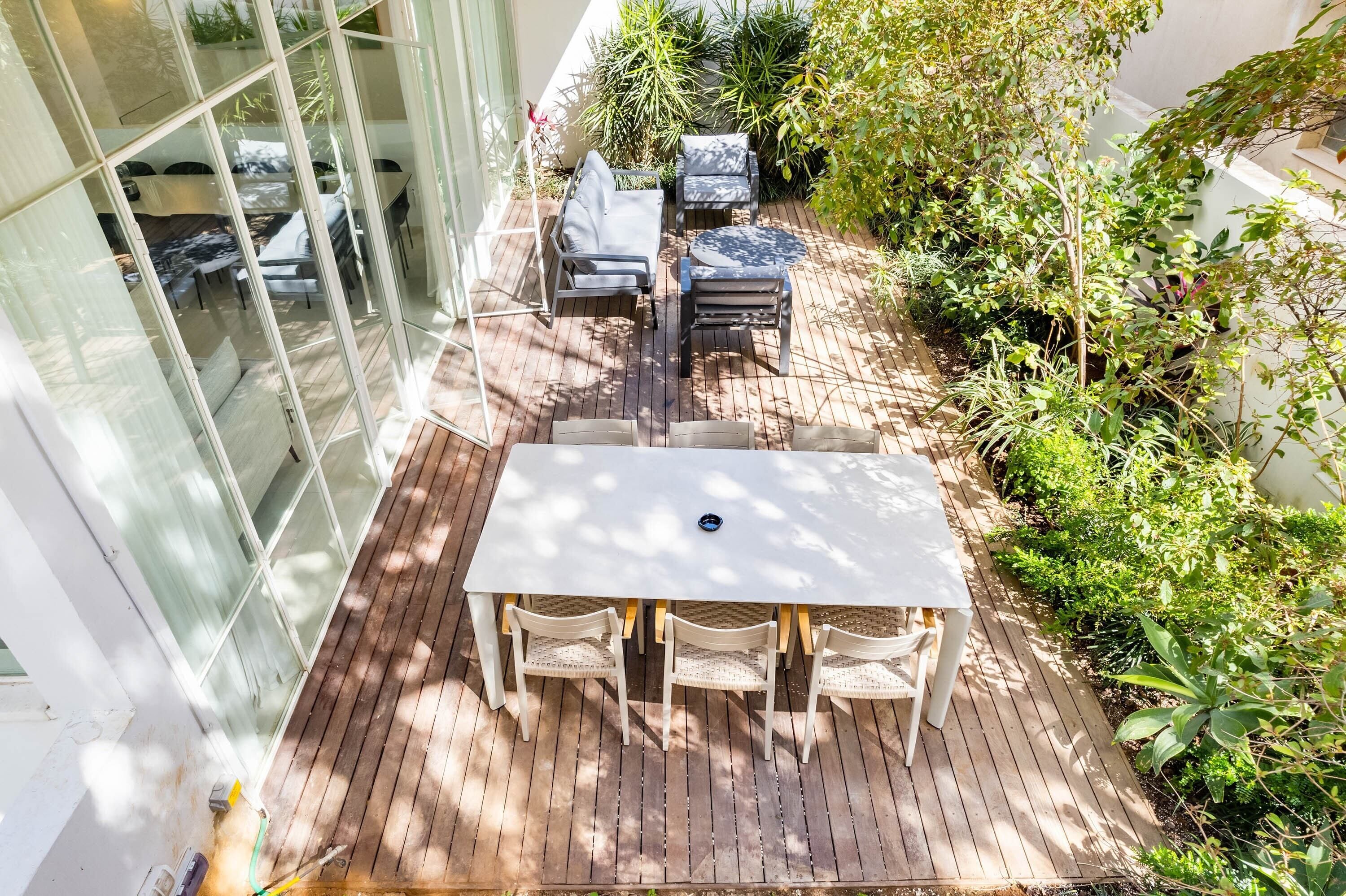Eine Terrasse mit Tisch und Stühlen, umgeben von üppiger Bepflanzung und einer Glaswand.