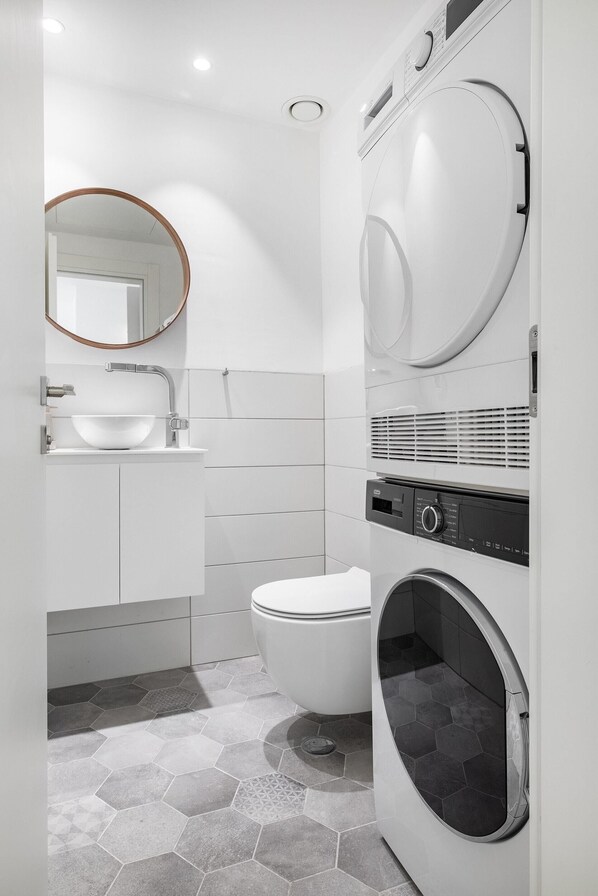 A modern bathroom with a white sink, toilet, and a built-in washing machine. - KG4 LUX Apartments (Tel Aviv)