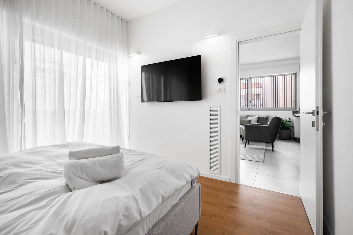 Ein modernes Hotelzimmer mit einem großen Bett, einem flachbildfernseher an der Wand und Blick auf den Außenbereich durch eine offene Tür.