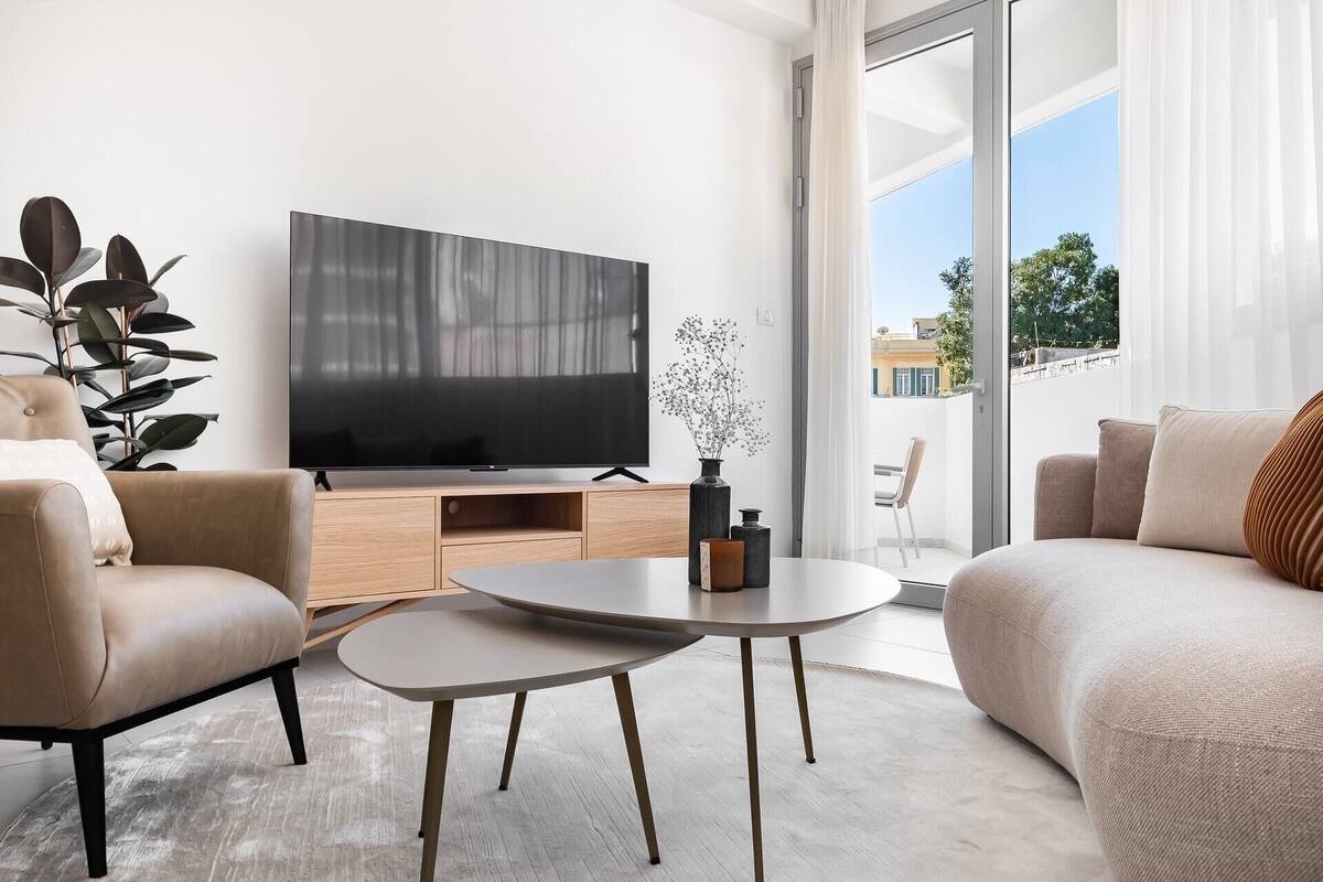 Ein modernes Wohnzimmer mit Fernseher, zwei Sofas, einem Couchtisch und einer großen Pflanze.
