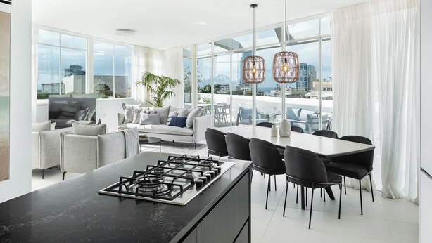 A modern kitchen with a gas stove, dining area with chairs, and large windows offering city views.