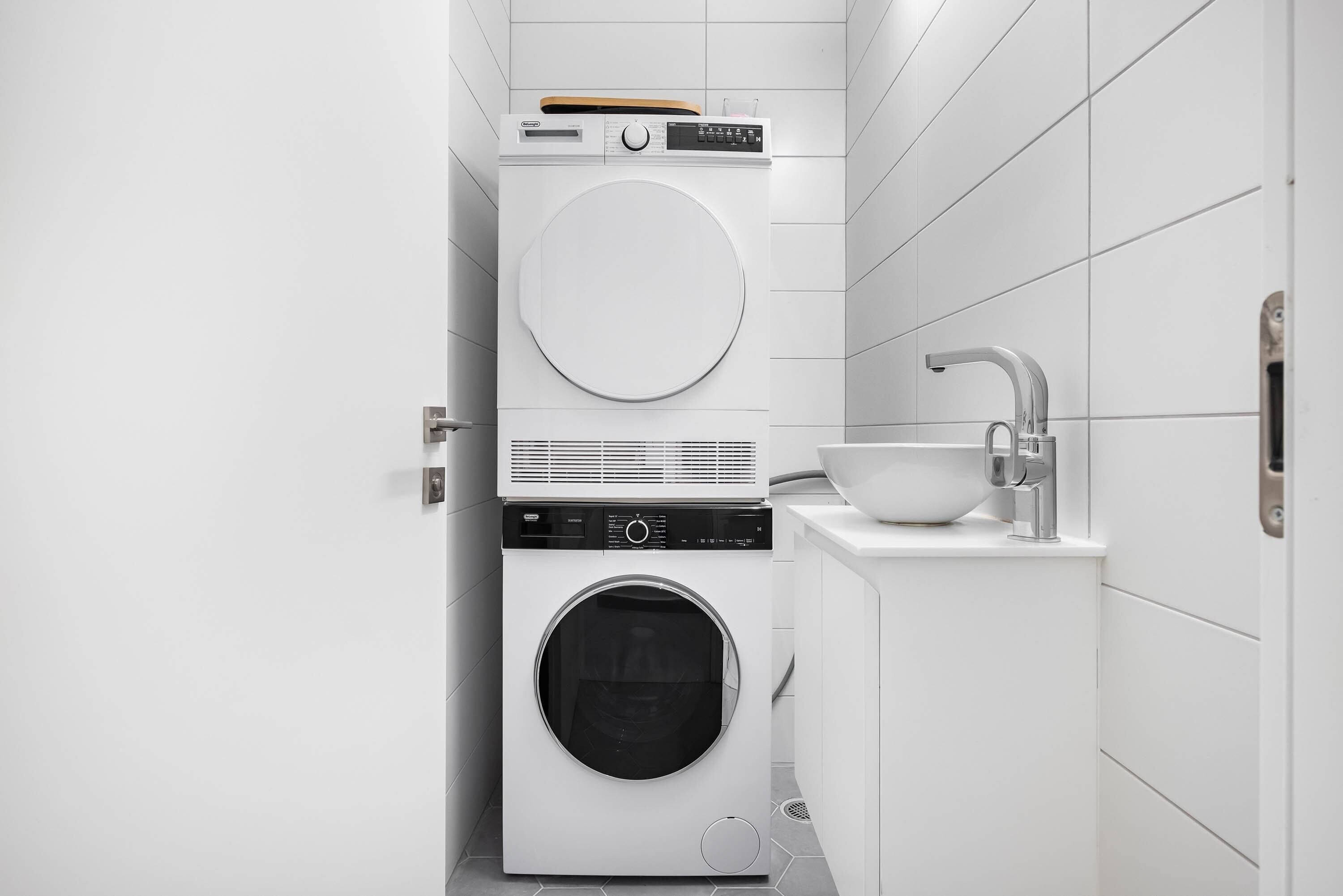 A compact laundry area with a front-loading washer and dryer, a sink, and a towel rack.
