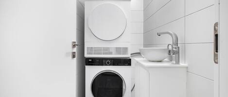 A compact laundry area with a front-loading washer and dryer, a sink, and a towel rack.