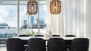 A modern dining area with a large table and black chairs, large windows with a city view, and two hanging wicker chandeliers.