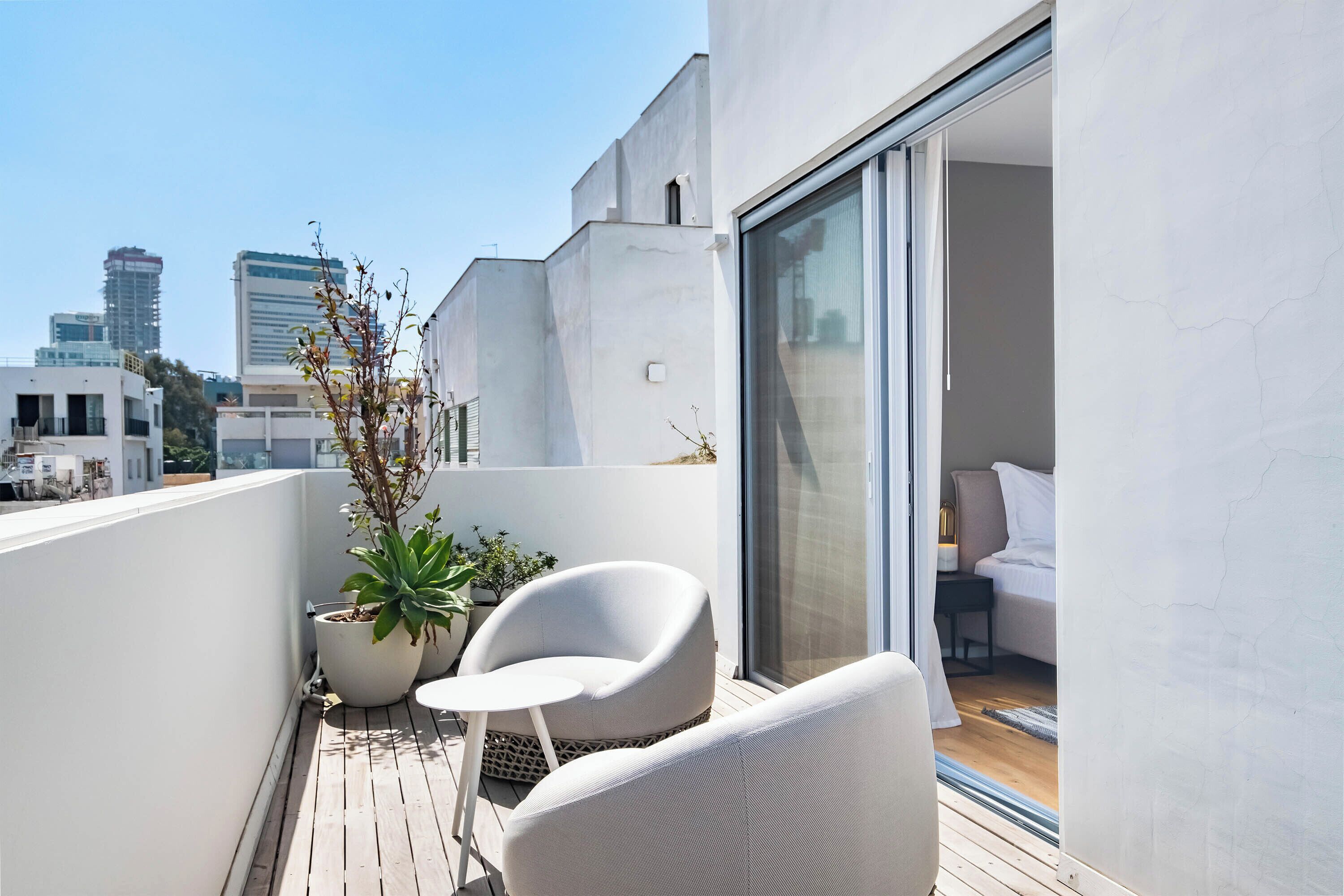 A modern balcony with a white chair, a small table, and a potted plant.