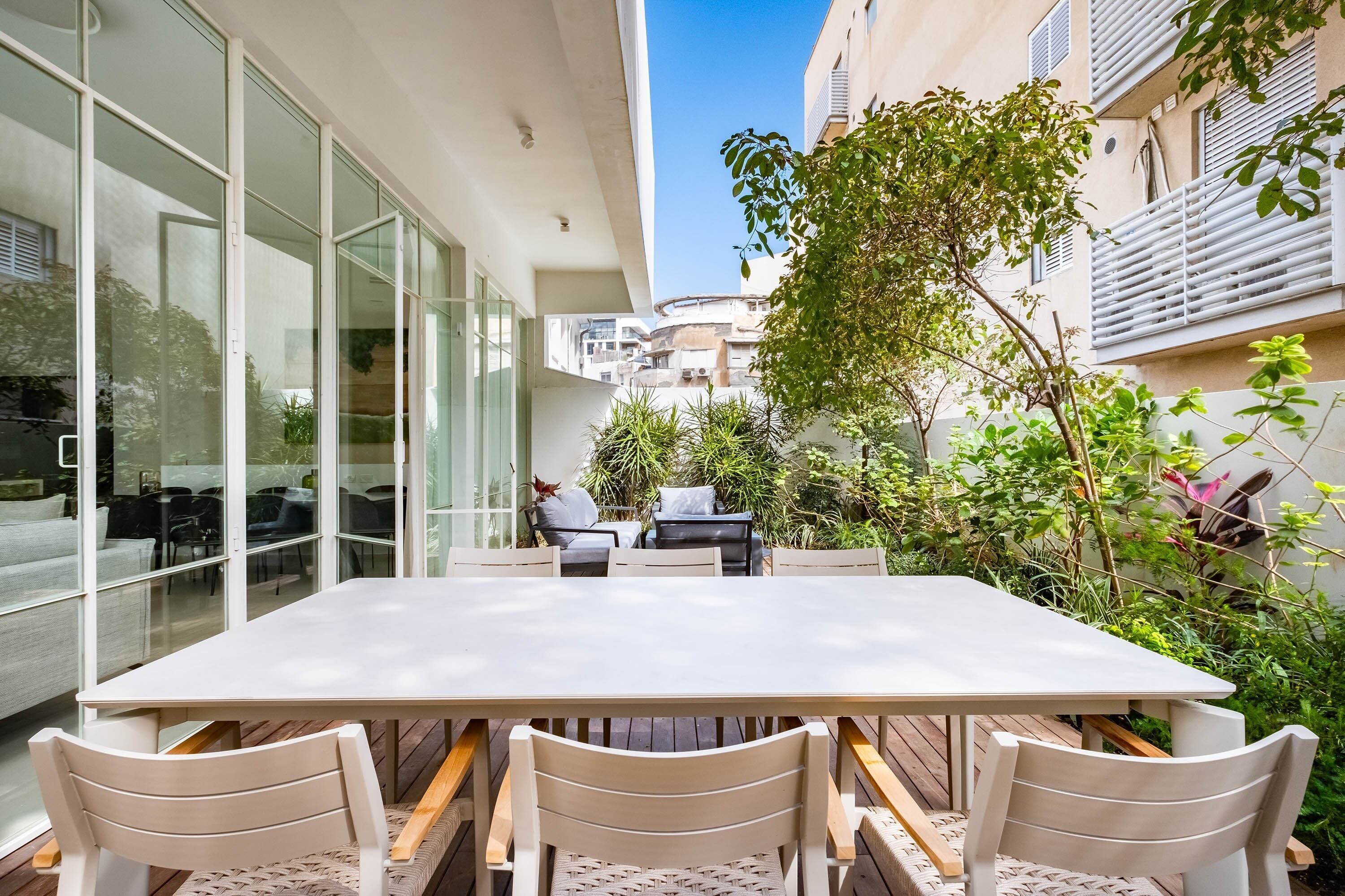 A modern outdoor patio with a dining table and chairs, surrounded by glass walls and greenery.