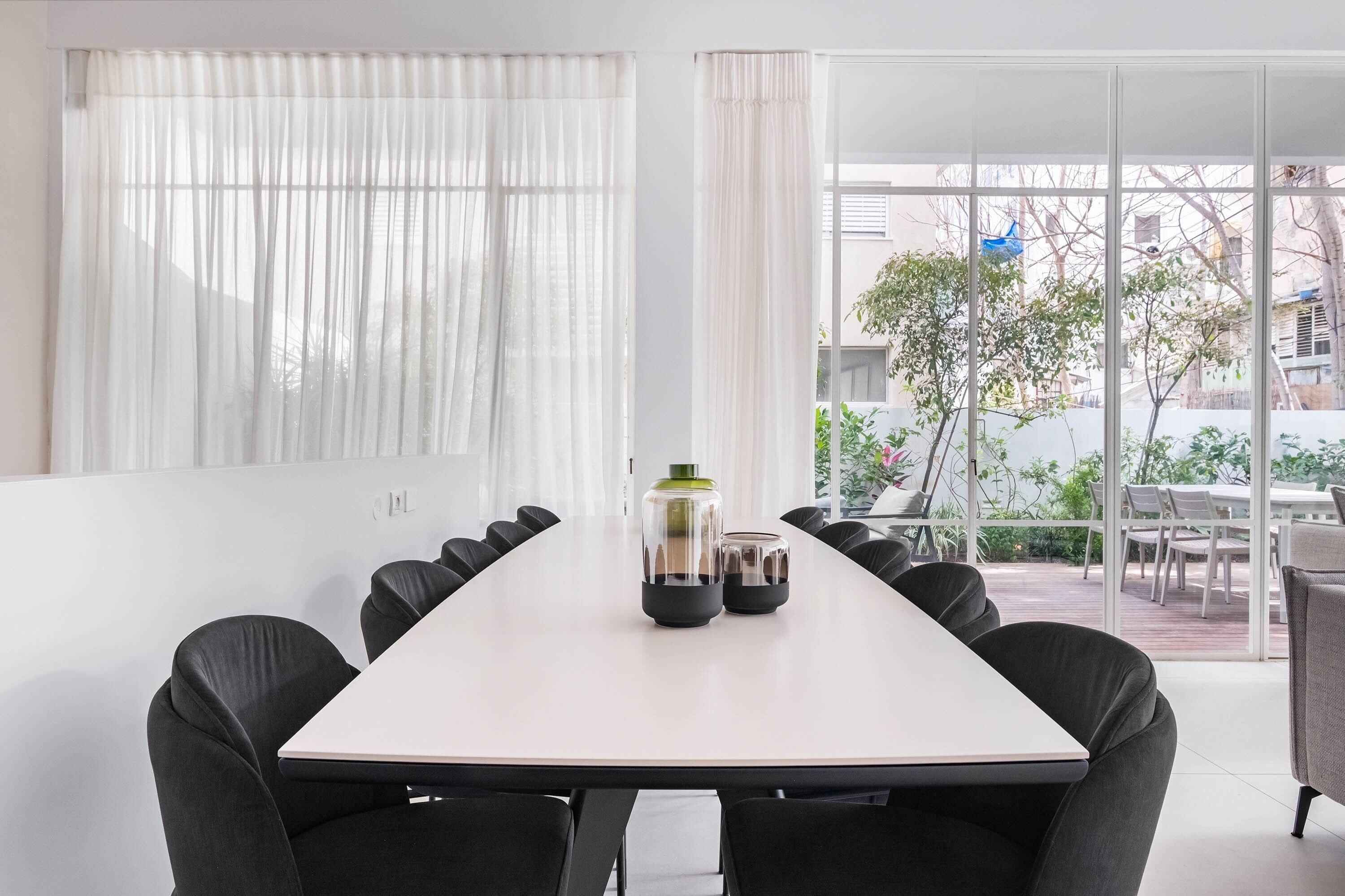 Een vergaderruimte met een lange tafel, zwarte stoelen en een glazen bijzettafel met decoratieve objecten.
