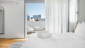 A hotel room with a large bed, a view of the cityscape, and a balcony with a table and chairs.