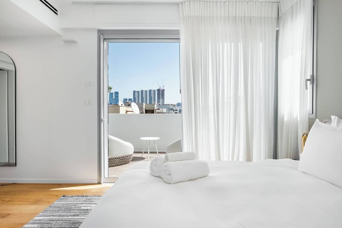 Ein Hotelzimmer mit einem großen Bett, Blick auf die Stadt und einem Balkon mit Tisch und Stühlen.