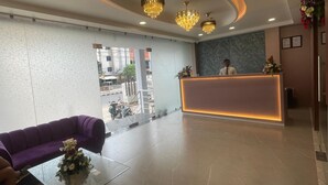 Zona de recepción de hotel con diseño moderno, que incluye un mostrador de recepción, un sofá morado y una mesa de vidrio con un centro de mesa floral.