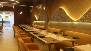 Un restaurante con mesas largas y cabinas, diseños geométricos en las paredes, y una persona visible al fondo.