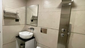 Un baño moderno con lavamanos blanco, espejo y cabina de ducha de acero inoxidable.