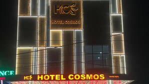 Un hotel llamado 'HOTEL COSMOS' con una fachada moderna y paneles iluminados.