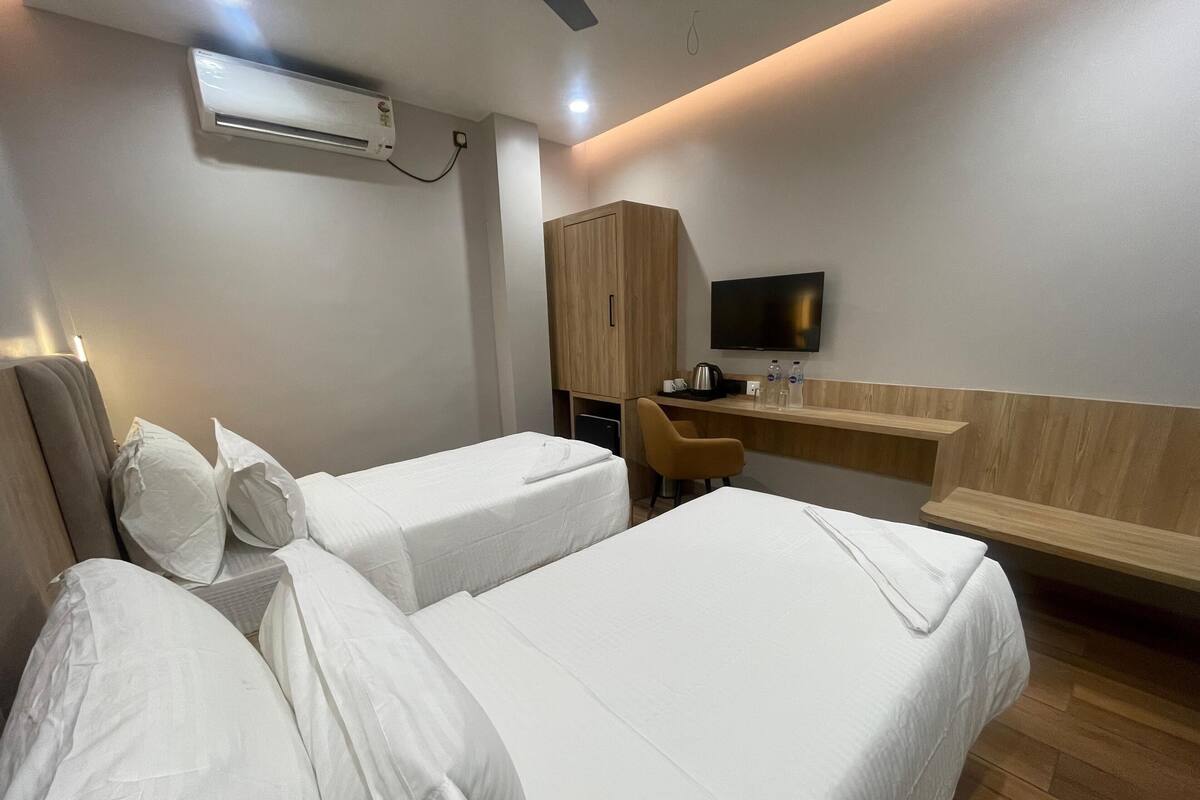 A hotel room with two single beds, a desk, a chair, a television, and an air conditioning unit.