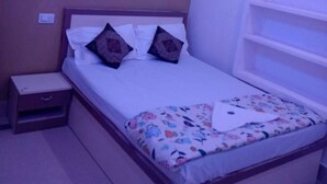 A bedroom with a bed, bedside table, and a ceiling fan. - Rudra Guest House (Varanasi)