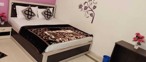 Un dormitorio con cama, mesita de noche, cómoda, decoración en la pared y una pequeña mesa con flores.