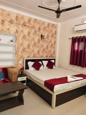A bedroom with a bed, a nightstand, a bedside table, a ceiling fan, and a wall-mounted air conditioner. - Rudra Guest House (Varanasi)
