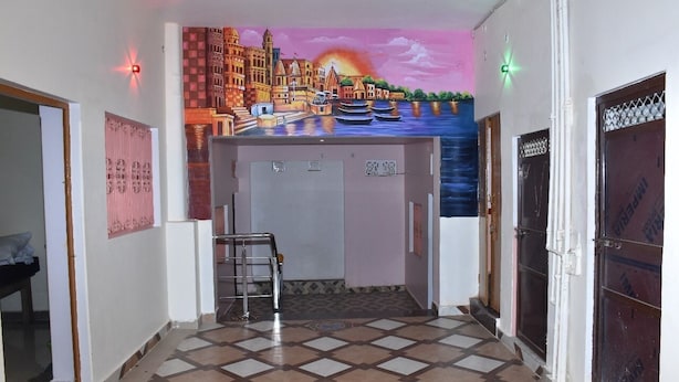A hallway with a tiled floor, a wheelchair, and a mural of a riverside scene on the wall. - Rudra Guest House (Varanasi)
