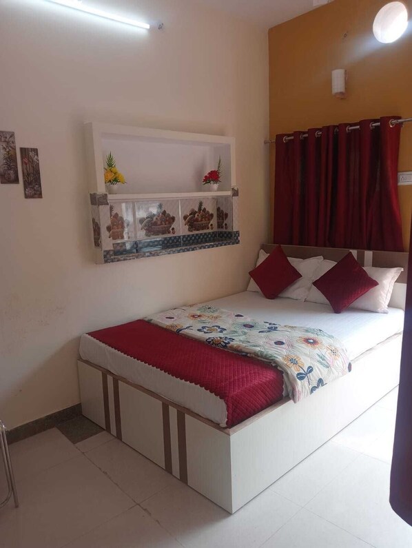 A bedroom with a bed, a shelf with decorative items, and a red curtain. - Rudra Guest House (Varanasi)