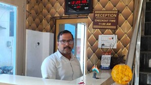 A reception desk with a digital clock displaying the time and date, a reception sign indicating check-out time, and a small Indian flag ornament. - Rudra Guest House (Varanasi)