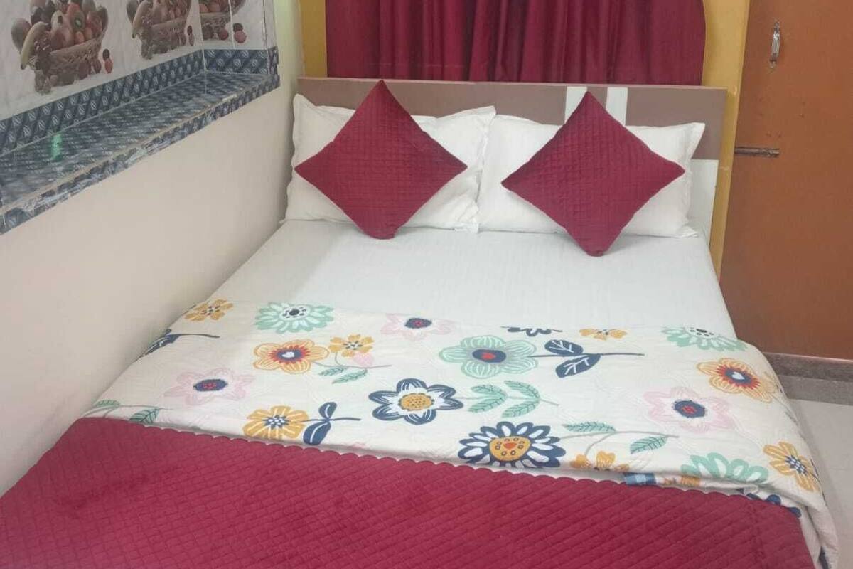 Una cama con una colcha estampada, dos almohadas y una manta roja.