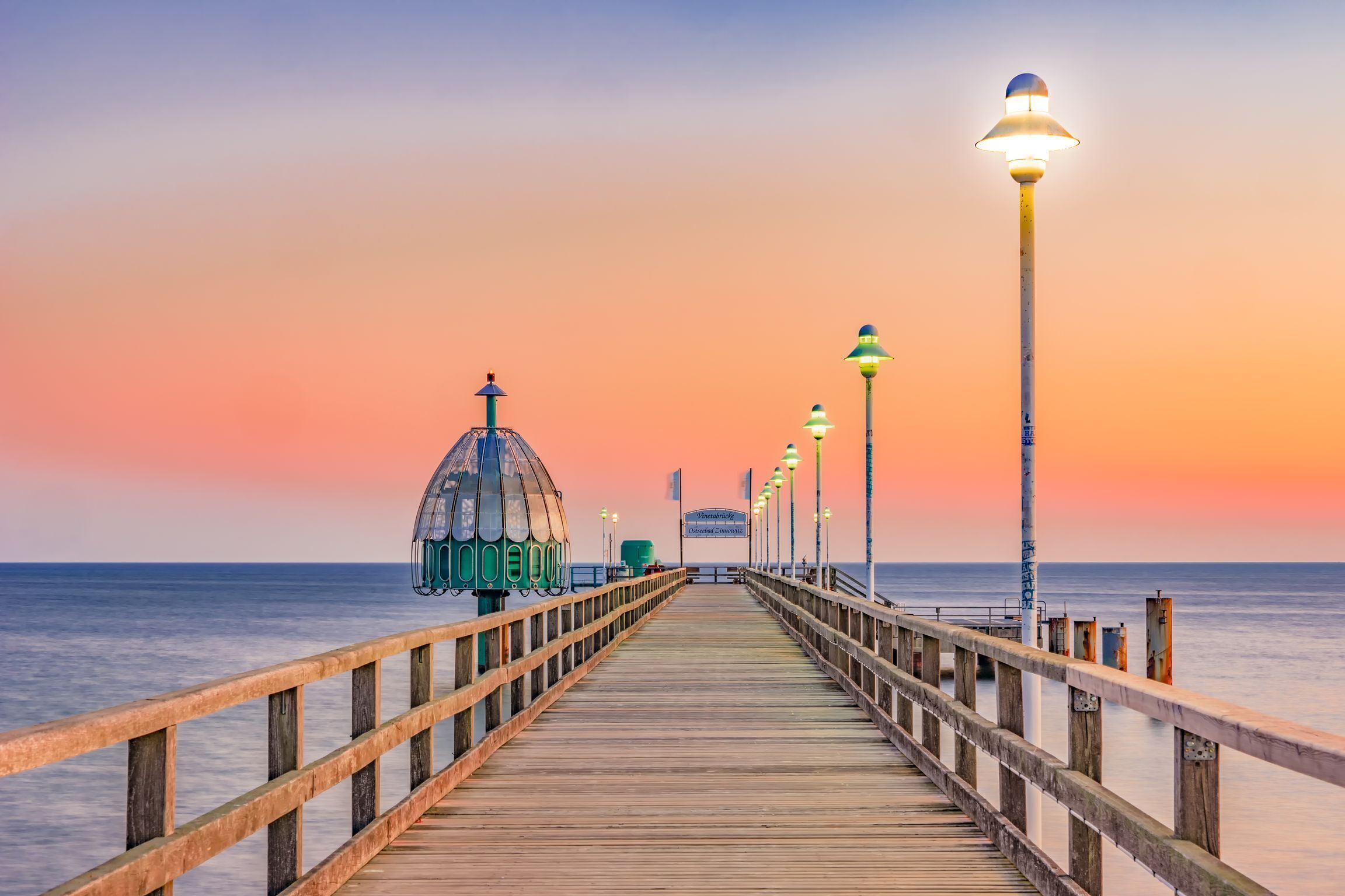 A wooden pier extending into the water with a gazebo and street lamps.