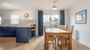 A modern kitchen with a central island, wooden dining table, and chairs. - Beachcomb Cottage | Elie (Elie)