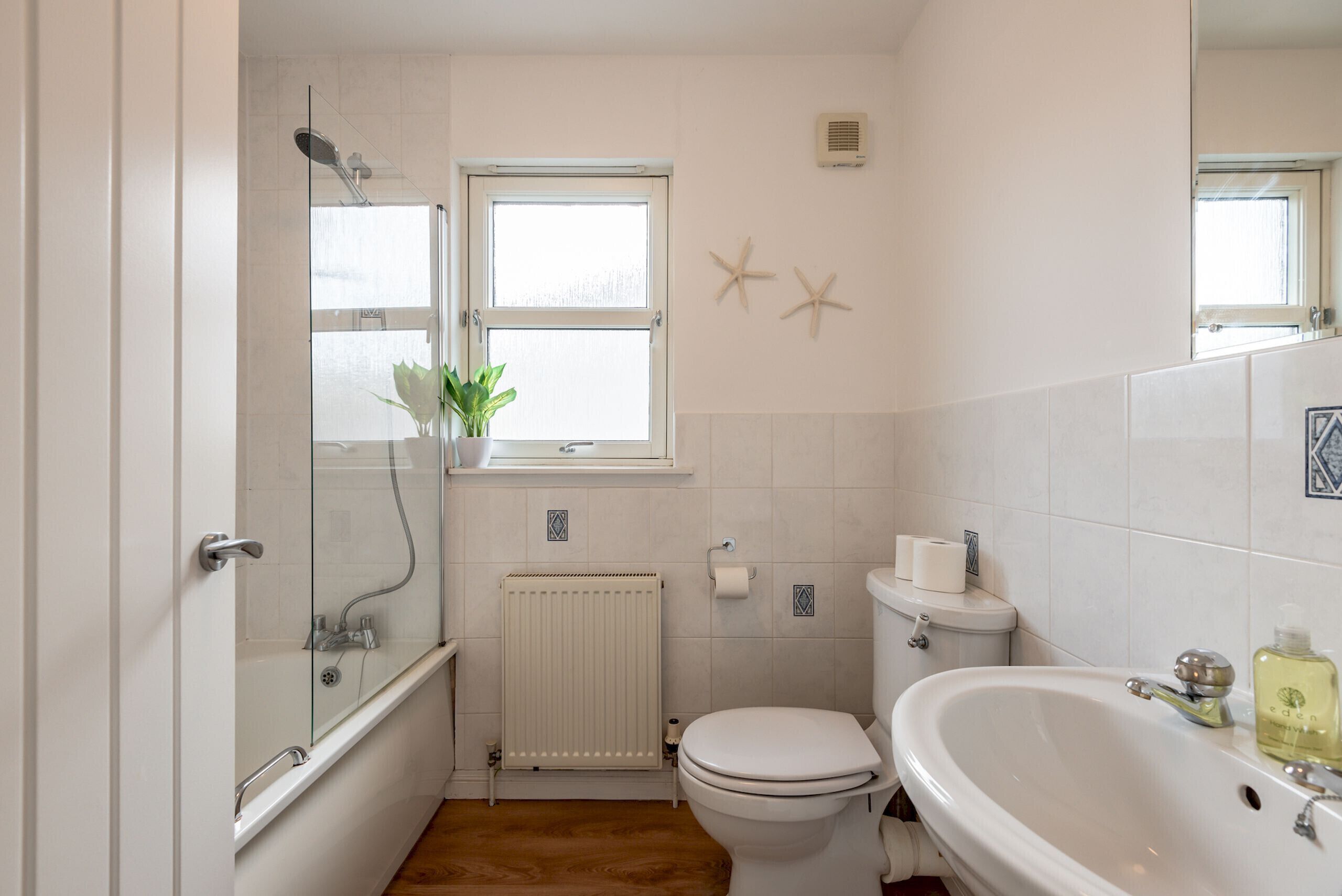 Ein Badezimmer mit Dusche, Toilette und Waschbecken, einem Fenster und dekorativen Seesternen an der Wand.