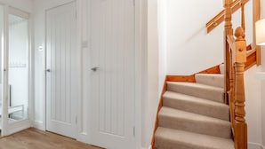 A staircase with wooden balusters and beige carpeted steps, adjacent to a white door with a glass panel. - Beachcomb Cottage | Elie (Elie)