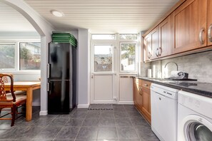 A modern kitchen with a black refrigerator, wooden cabinets, a built-in dishwasher, and a dining area with a wooden table and chairs.