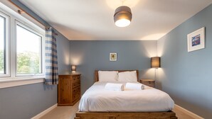 Camera da letto con un letto in legno, un comodino, una cassettiera, una finestra con tende e una lampada a parete.