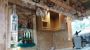 A bar area with wooden beams, wine bottles, and hanging glassware.