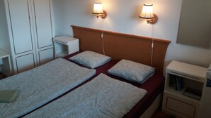 A bedroom with a bed, two bedside lamps, a nightstand, a wardrobe, and a small shelf with books.