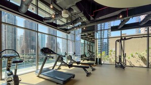 Un gimnasio con cintas de correr, bicicletas estáticas y máquinas de pesas, ventanas amplias y vistas a rascacielos.