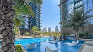 Un área de piscina moderna en un hotel, con agua azul cristalina, rodeada de palmeras y edificios contemporáneos.