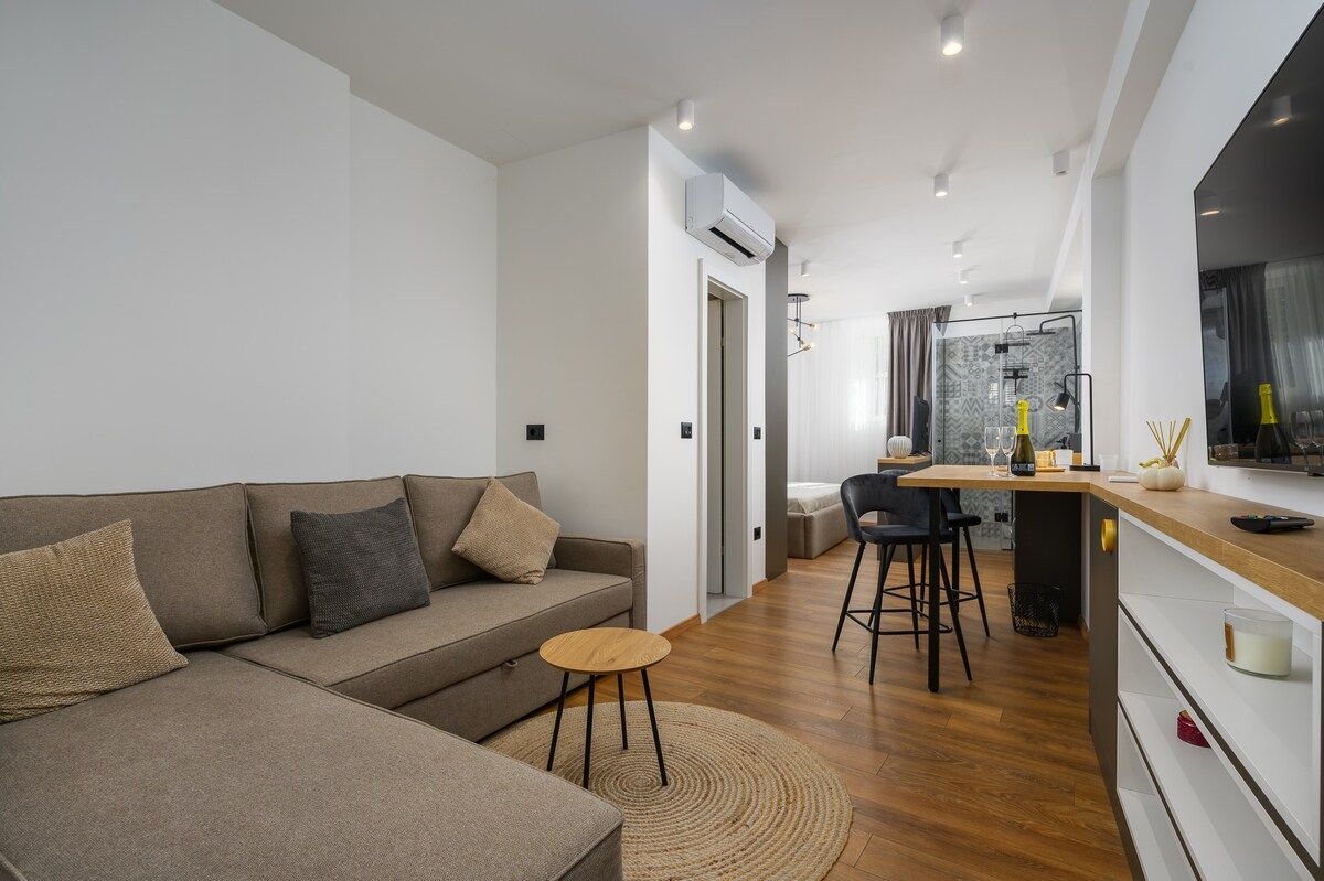 Ein stilvoller Wohnbereich mit Sofa, einem kleinen runden Tisch und einer Küchenzeile mit Bar.