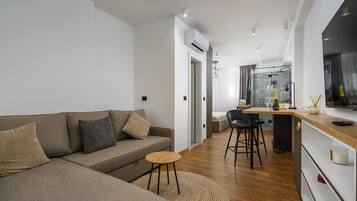 En moderne stue med sofa, et lille rundt bord og et tekøkken med bardisk.
