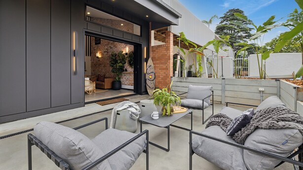 Un patio al aire libre con mobiliario moderno, pared de ladrillo y plantas en macetas.