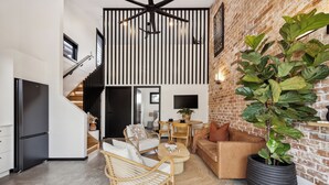 Una sala de estar moderna con una planta grande en maceta, un sofá, una mesita de centro y una silla de mimbre.