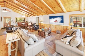 Un salón espacioso con techo de madera alto, un comedor con sillas de madera y un amplio ventanal con vistas.
